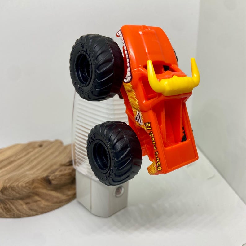 May include: An orange toy monster truck with black tyres and the text "El Toro Loco". The truck has yellow horns and a white and red design on the front. The toy is resting on a white night light.