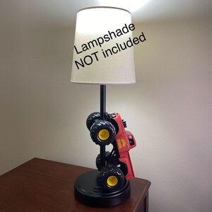 Może przedstawiać: Czerwona i czarna lampa w kształcie monster trucka z ż&oacute;łtymi akcentami. Lampa ma czarną podstawę i czarny słupek podtrzymujący beżowy abażur. Widoczny jest napis "Lampshade NOT included".