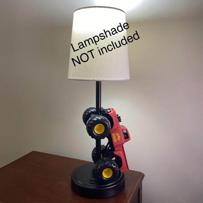 Może przedstawiać: Czerwona i czarna lampa w kształcie monster trucka z ż&oacute;łtymi akcentami. Lampa ma czarną podstawę i czarny słupek podtrzymujący beżowy abażur. Widoczny jest napis "Lampshade NOT included".