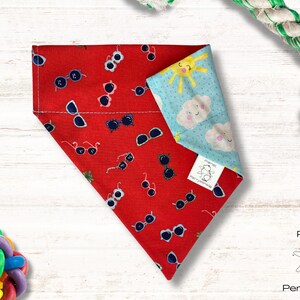 May include: Red bandana with a pattern of sunglasses and a sun and clouds design. The bandana is reversible and has a blue side with a sun and clouds design. The bandana is made by Planet Perrywinkle.
