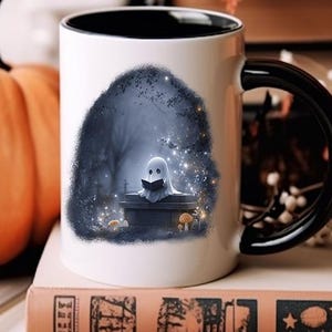 Puede incluir: Taza de cer&aacute;mica blanca con interior y asa negros. La taza presenta una ilustraci&oacute;n caprichosa de un fantasma leyendo un libro en un cementerio. Una calabaza es visible en el fondo, lo que sugiere un tema de Halloween.