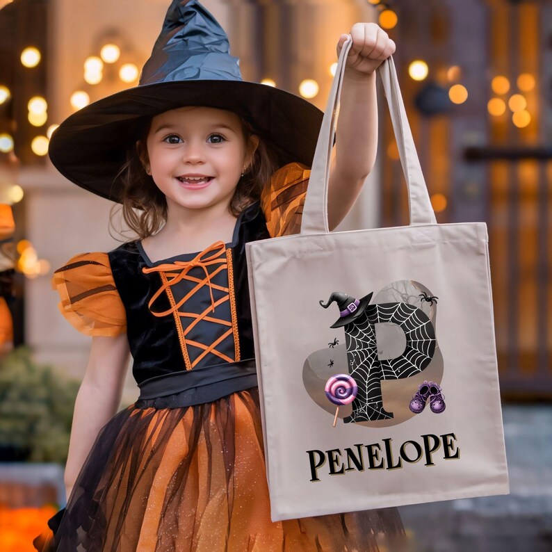 Peut inclure: Un sac en toile beige pour la cueillette de bonbons d'Halloween avec une toile d'araign&eacute;e noire et la lettre "P" au centre. Un chapeau de sorci&egrave;re est sur la lettre. Le sac porte le nom "PENELOPE" imprim&eacute; en bas. Une jeune fille d&eacute;guis&eacute;e en sorci&egrave;re tient le sac.