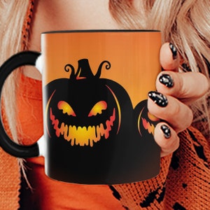 Puede incluir: Una taza de café negra con asa negra presenta un fondo naranja con una silueta de una calabaza tallada en forma de cara con una sonrisa que gotea y ojos brillantes.