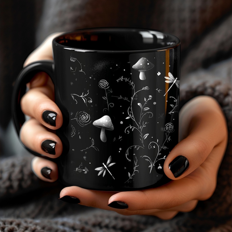 May include: Black ceramic mug featuring a whimsical design of white mushrooms, flowers, and dragonflies. The mug has a black handle and a glossy finish. The design is a delicate, nature-inspired illustration.