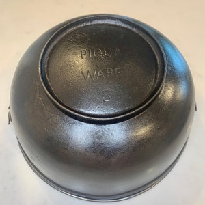 May include: Black cast iron pot with the words "PIQUA WARE" and the number "5" on the bottom.