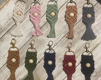 Puede incluir: Diez llaveros de macramé de colores con cuentas de madera. Cada llavero tiene un color diferente y una borla. Los llaveros se muestran en una superficie de madera.