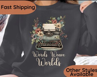 May include: A dark gray sweatshirt with a vintage typewriter and floral design. The text "Words Weave Worlds" is printed below the typewriter.  Other Styles Available.