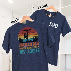 May include: Navy blue t-shirt with the word "Dad" and a stick figure family on the front. The back of the shirt features a graphic of a lineman on a utility pole with the text "Lineman Dad Like a Normal Dad Just Cooler."