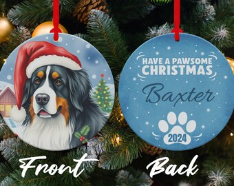 Può includere: Un ornamento natalizio rotondo con un cane da montagna bernese che indossa un cappello di Babbo Natale sul davanti. Il retro dell'ornamento dice "Have a Pawsome Christmas" con il nome "Baxter" e l'anno "2024" in un'impronta di zampa.