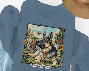 Puede incluir: Sudadera azul con un gráfico de un perro pastor alemán tumbado en un jardín con girasoles y una mariposa. Las palabras "GERMAN SHEPHERD" están impresas en la parte inferior del gráfico.