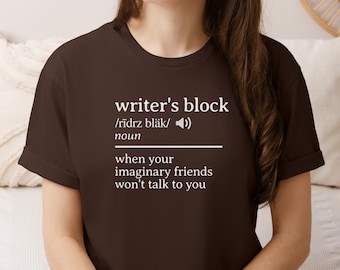 May include: A brown t-shirt with the words "writer's block" in white, along with a phonetic pronunciation and definition. The definition reads "when your imaginary friends won't talk to you."
