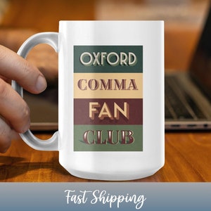 Puede incluir: Taza de cerámica blanca con el texto "OXFORD COMMA FAN CLUB" en una fuente de estilo vintage. El texto está superpuesto a un fondo de rayas verdes, beige y granate. La taza tiene un asa blanca y la sostiene una persona.