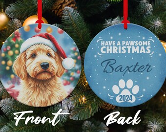 Może przedstawiać: Okrągła ozdoba choinkowa z obrazkiem psa w czapce Świętego Mikołaja z przodu. Z tyłu ozdoby napis "Have a Pawsome Christmas" z imieniem "Baxter" i rokiem "2024" nadrukowanym na niej.