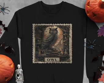Può includere: Felpa nera con una dettagliata illustrazione di un gufo all'interno di una cornice vintage. L'opera d'arte include uno sfondo spettrale con una luna piena, teschi e la parola "OWL". Abbigliamento a tema Halloween. Il design ricorda un francobollo vintage.