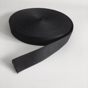 Könnte beinhalten: Eine Rolle schwarzes Nylonband, eine Art von starkem, strapazierfähigem Stoff, der oft für Gurte, Gürtel und andere Anwendungen verwendet wird.