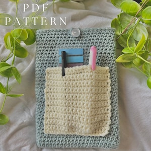 May include: A crocheted teal pouch with a white crocheted pocket inside. The pouch has a button closure and is filled with a pink highlighter and a black pen.
