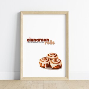 Puede incluir: Una impresión enmarcada con el texto "cinnamon rolls" y el lema "a swirl of happiness on a plate". La impresión presenta una ilustración digital de tres rollos de canela con glaseado blanco.
