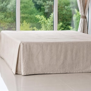 May include: A solid light beige bed skirt with a tailored design featuring clean, straight lines and a smooth, flat surface that drapes down to the floor, providing a uniform and structured appearance around the base of a bed frame.