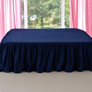 Könnte beinhalten: Ein einfarbiger, marineblauer Bettvolant mit gerafftem Rüschendesign, das von der Oberseite bis zum Boden reicht. Der Stoff hat eine matte Textur und bedeckt den Bettrahmen vollständig mit gleichmäßigen Falten entlang der Seiten.