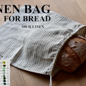 Pode incluir: Uma bolsa de pão de linho branco com listras cinzas. A bolsa é feita de 100% linho e tem um fecho de cordão. A bolsa está cheia de um pão. O texto "LINEN BAG FOR BREAD 100% LINEN" está impresso na bolsa. O texto "ALL COLORS COLORS GUIDE" está impresso em um pequeno cartão com uma tabela de cores.