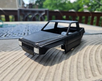 Op de afbeelding: Zwart plastic model truck chassis zonder wielen of interieur. De truck is een pick-up truck met een laadbak achterin. De truck staat op een houten oppervlak.