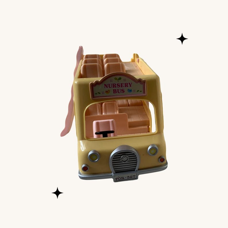 May include: A yellow toy bus with a pink interior and the words "Nursery Bus" on the front. The bus has a sign that says "For 381T".