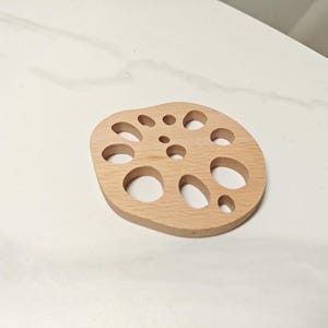 May include: A wooden coaster with a lotus flower design. The coaster has multiple circular cutouts.