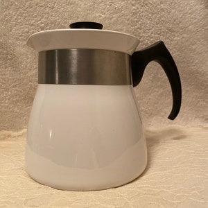 May include: White ceramic coffee pot with a stainless steel band and a black handle.