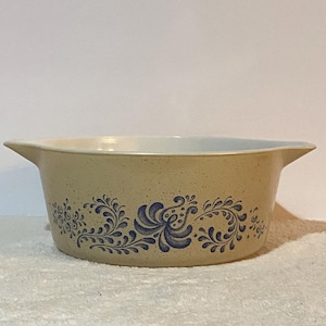 May include: Tan stoneware casserole dish with blue floral design. The dish has a rounded shape with two handles and a white interior. The blue floral pattern wraps around the exterior of the dish.