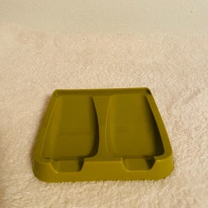 May include: A green plastic dish with two indented sections for holding utensils.