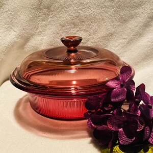 May include: A vintage red glass baking dish with a lid. The dish has a ribbed design and the lid has a knob on top.
