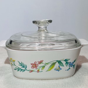 May include: White casserole dish with a clear glass lid. The dish is decorated with a floral pattern in shades of pink, yellow, blue, and green. The dish has two white handles.