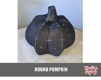 May include: A black, round pumpkin with white markings and a stem. The pumpkin is sitting on a light brown, wooden surface. The text "ROUND PUMPKIN" is at the bottom of the image.