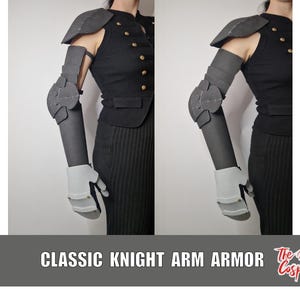 Puede incluir: Un conjunto de armadura de brazo articulada de color gris oscuro que incluye hombrera, protector de brazo, coderas, protector de antebrazo y una placa de mano gris claro. La armadura se lleva sobre un chaleco negro sin mangas con botones dorados.