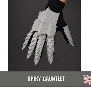 Puede incluir: Un guante negro con placas de armadura de color gris claro, superpuestas y puntiagudas, que cubren el dorso de la mano y los dedos. La armadura tiene un diseño afilado y espinoso. El texto "SPIKY GAUNTLET" y "The Dodo Cosplay" aparece abajo.