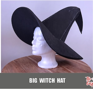 Könnte beinhalten: Ein großer schwarzer Hexenhut mit einer breiten, geschwungenen Krempe und einer hohen, spitzen Krone. Der Hut wird auf einem weißen Schaufensterpuppenkopf präsentiert. Der Text "BIG WITCH HAT" ist unten in weißen Großbuchstaben gedruckt, neben dem Logo "The Dodo Cosplay".