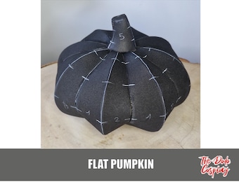 May include: A black, flat pumpkin with white stitching and numbered markings. The pumpkin is sitting on a wooden surface. The text "FLAT PUMPKIN" is displayed in white block letters at the bottom of the image.