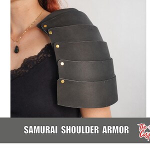 May include: A black layered shoulder armor piece featuring five overlapping curved plates secured with gold-toned metal rivets. The armor is worn over a black top with lace trim. The text SAMURAI SHOULDER ARMOR and The Dodo Cosplay are visible.