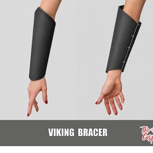 Könnte beinhalten: Ein Paar schwarze Unterarmschienen mit glatter, matter Oberfläche und weißen Nähten entlang der Seitennaht. Der Text VIKING BRACER und The Dodo Cosplay ist unten im Bild auf einem dunkelgrauen horizontalen Banner aufgedruckt.