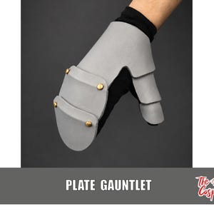 May include: A light gray plate gauntlet featuring layered armor segments secured with gold-toned metal rivets. The gauntlet is worn over a black fabric glove, covering the back of the hand and the thumb, with the text PLATE GAUNTLET visible below.