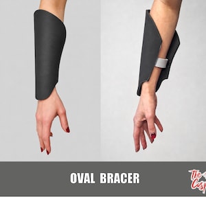 May include: A matte black forearm bracer featuring a smooth, curved design that wraps around the arm. The bracer is secured with a white strap on the inner side. The text OVAL BRACER and The Dodo Cosplay are visible at the bottom of the image.