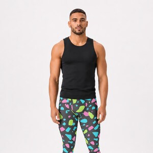 May include: A black sleeveless tank top paired with fitted leggings featuring a dark gray base and a scattered terrazzo-style pattern in vibrant shades of neon pink, bright blue, and lime green, completed by white athletic sneakers.