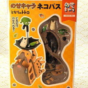 May include: A boxed set of Studio Ghibli figures featuring characters from "My Neighbor Totoro." The set includes a Catbus figure, Totoro, and other characters. The box is orange with Japanese text and illustrations.