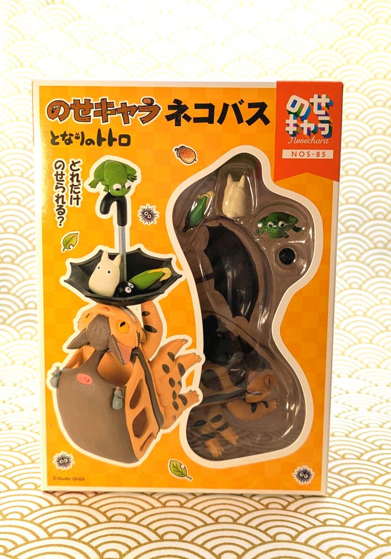 May include: A boxed set of Studio Ghibli figures featuring characters from "My Neighbor Totoro." The set includes a Catbus figure, Totoro, and other characters. The box is orange with Japanese text and illustrations.