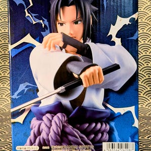 Pode incluir: Figura Grandista de um personagem de anime masculino em um traje branco e azul, segurando uma arma preta. A figura tem cabelo preto e est&aacute; em um fundo azul com desenhos de raios. A caixa tem o logotipo Grandista.