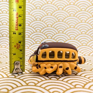 May include: A yellow and brown toy bus with cat-like legs. The bus has a brown roof and windows. The toy is about 3 inches long.