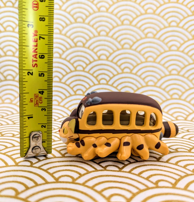 May include: A yellow and brown toy bus with cat-like legs. The bus has a brown roof and windows. The toy is about 3 inches long.