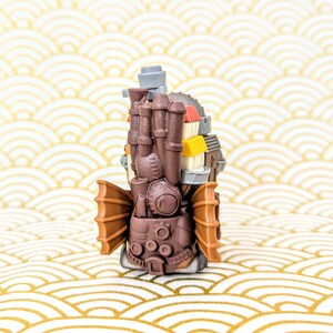 Peut inclure: Figurine d&eacute;taill&eacute;e de style steampunk marron, avec plusieurs chemin&eacute;es, petites maisons et structures en forme d'ailes. La figurine pr&eacute;sente un design complexe avec diverses formes et textures, sur fond &agrave; motifs.