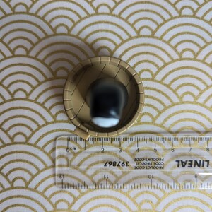 May include: A small, round, brown ceramic bowl with a black and white design inside. The bowl is sitting on a white and gold patterned surface.