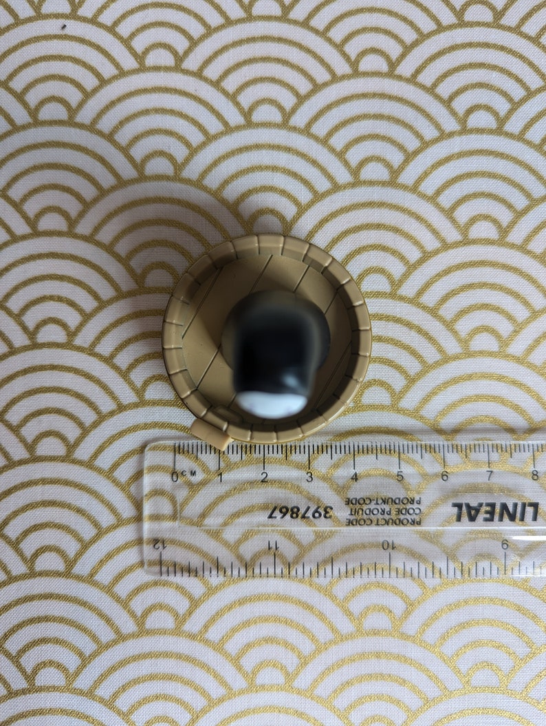 May include: A small, round, brown ceramic bowl with a black and white design inside. The bowl is sitting on a white and gold patterned surface.